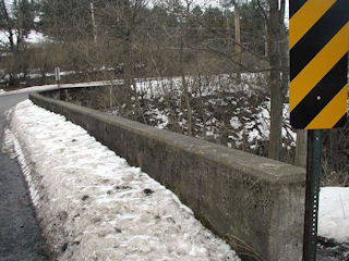 The marker located just behind the sign, and plenty of leftover snow on a gray and windy day.