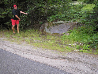 Rich holds back the tree branches to show the mark and the outcrop.