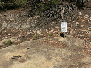 Eyelevel view of mark on outcrop, with witness post in the background.