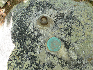 Eyelevel view of the triangulation station disk and a strange post in the boulder.