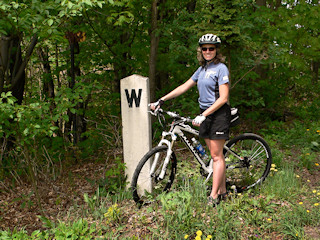 Zhanna stands next to a well preserved whistle post near a road crossing.