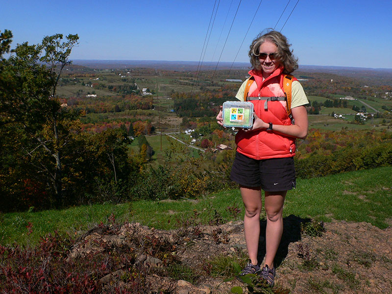 Zhanna displays the cache against a colorful panoramic backdrop.